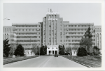 Black and white image of Fitzsimons Army Medical Center with a tree lined road in front of it.