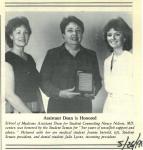Newspaper clipping featuring a black and white photo of three smiling dark-haired women in dresses with the woman in the center holding an award. The caption underneath reads Assistant Dean is Honored.