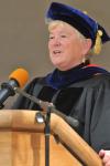 Maureen Garrity wearing academic regalia standing behind a wooden podium with a microphone.