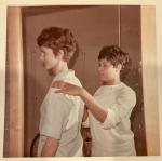 During an exercise for their physical therapy program, a female student with short brown hair stands with her back to the camera while LaRae Kemp in a white uniform, places her hands on the student's shoulders.
