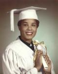 LaRae Kemp in a white graduation cap and gown holding a diploma with a gold ribbon wrapped around it.  