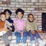 Four of LaRae Kemp's young children sitting on the hearth of a brick fireplace.