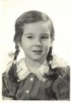 Black-and-white portrait of a young girl with brown pigtails wearing a collared button-up shirt with lace trim.