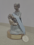 Bronze Nightingale Award statue of a seated woman in a long dress holding a patient on her lap, clasping hands as they look at each other.