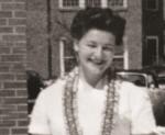 Black and white portrait of a smiling Dr. Bonnie Camp in a white blouse with black lace trim in front of a brick building.
