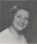 Black-and-white portrait of a smiling Bonnie Camp with short, curled hair, wearing a necklace and light-colored sweater, posed against a plain studio background.