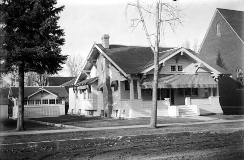 Black and white photo of a two-storied house with a front porch, striped awnings, and a detached garage.