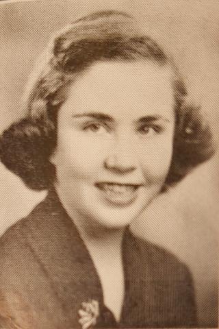 Sepia-toned portrait of a young woman with wavy brown hair. She is wearing a dark jacket with a floral pin, suggesting a yearbook photo from the mid-20th century.