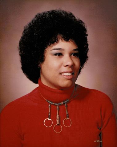 LaRae Kemp wearing a red turtleneck with a necklace that has three circular metal hoops.