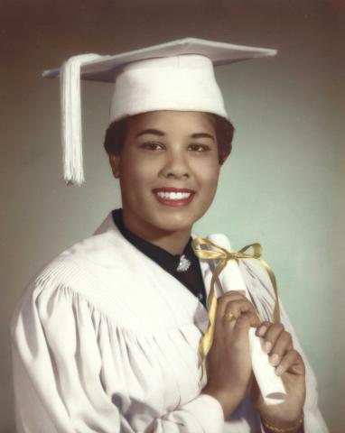 LaRae Kemp in a white graduation cap and gown holding a diploma with a gold ribbon wrapped around it.  