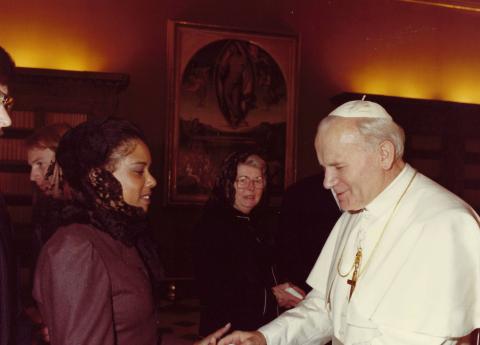 LaRae Kemp in a dark jacket and black lace head scarf shaking hands with Pope John Paul II in the 1980s.