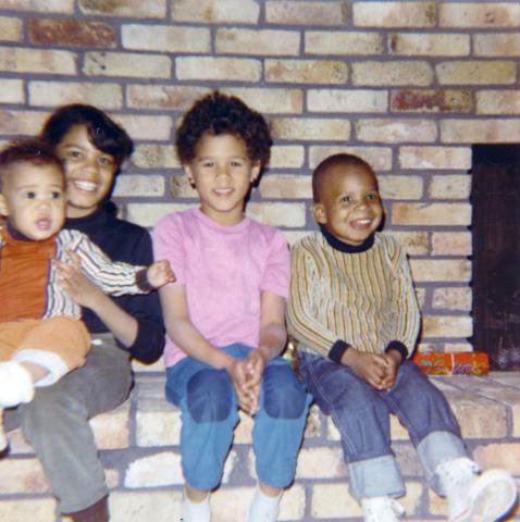 Four of LaRae Kemp's young children sitting on the hearth of a brick fireplace.
