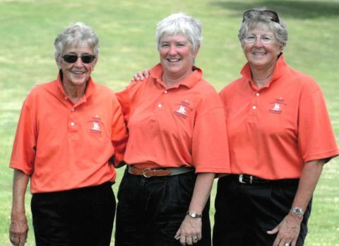 Maureen , center, with two other women wearing matching orange polo shirts and black pants, standing on a golf course.