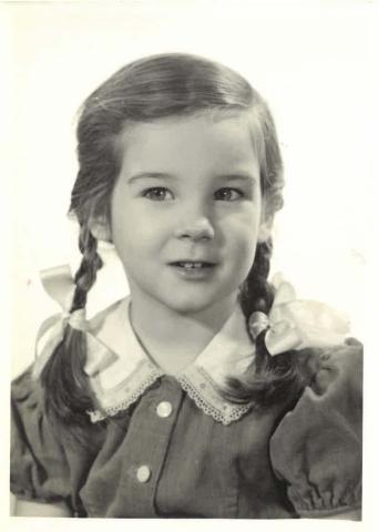 Black-and-white portrait of a young girl with brown pigtails wearing a collared button-up shirt with lace trim.
