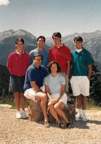 The Krugman family at a scenic mountain overlook; Mary and Dick sit on a rock while their four sons stand behind them in casual attire.