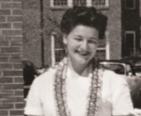 Black and white portrait of a smiling Dr. Bonnie Camp in a white blouse with black lace trim in front of a brick building.