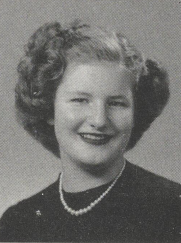Black-and-white portrait of a smiling Bonnie Camp with short, curled hair, wearing a necklace and dark-colored top, posed against a plain studio background.