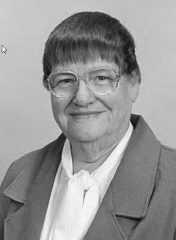 Dr. Bonnie Camp with short dark hair wearing round framed glasses and a white blouse and dark-colored blazer.