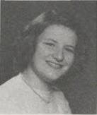 Black-and-white portrait of a smiling Bonnie Camp with short, curled hair, wearing a necklace and light-colored sweater, posed against a plain studio background.