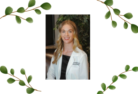 Danielle Jenkins, AuD with long blond wavy and blue eyes wearing a black blouse under a white lab coat.