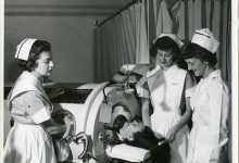 Three female nurses standing around an iron lung with a patient, circa 1950's.