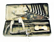 Metal box with a button latch. Inside the lid are two long instruments.