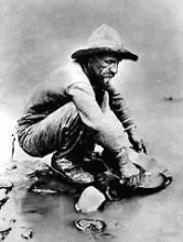 Man kneeling down panning for gold.
