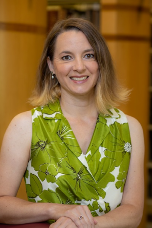 Kristen DeSanto posing in a library wearing a green and white short-sleeved shirt.