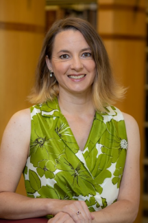 Kristen DeSanto posing in a library wearing a green and white short-sleeved shirt.