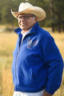 Spero M. Manson, Ph.D. wearing a white cowboy hat with a royal blue coat standing in a field smiling.